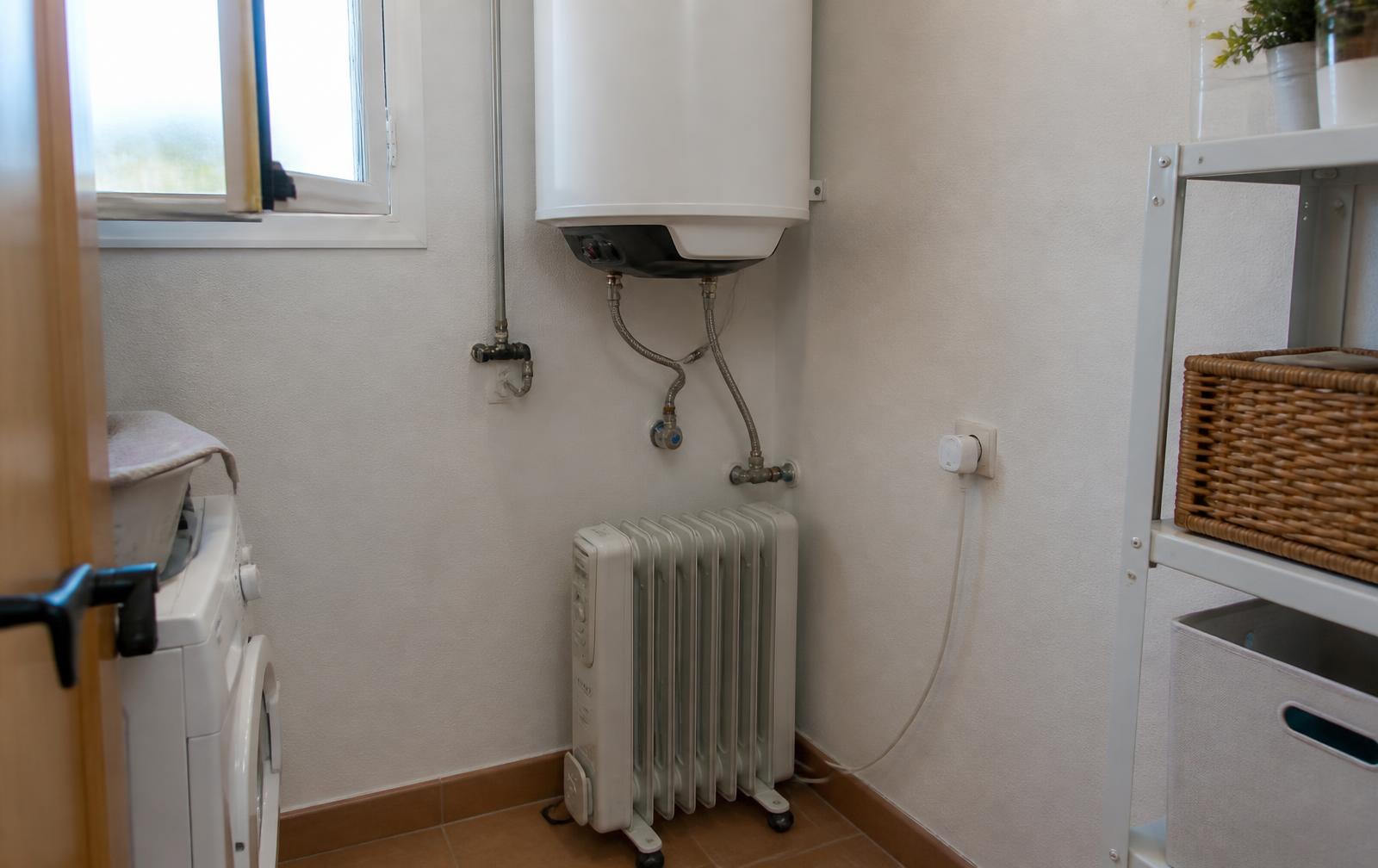 Termo eléctrico y radiador en un cuarto de instalaciones con un enchufe inteligente en la pared